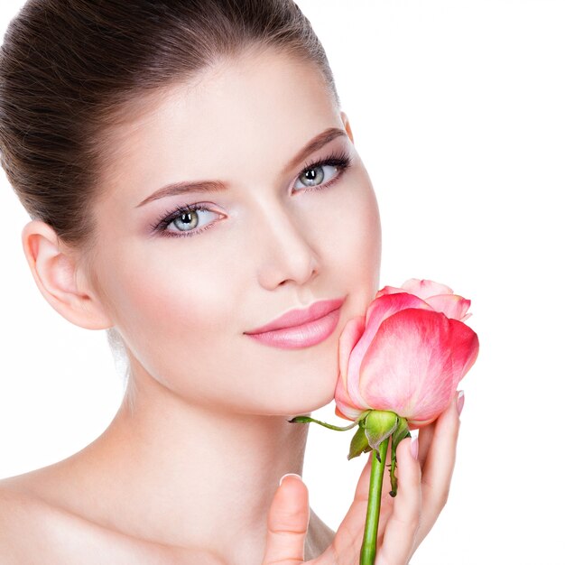 Closeup retrato de mujer joven hermosa con piel sana y flor cerca de la cara - aislado en blanco.