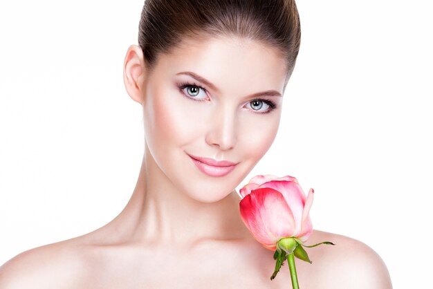 Closeup retrato de mujer joven hermosa con piel sana y flor cerca de la cara - aislado en blanco.