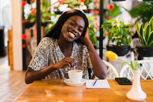 Closeup retrato de mujer negra joven feliz tomando café en la cafetería