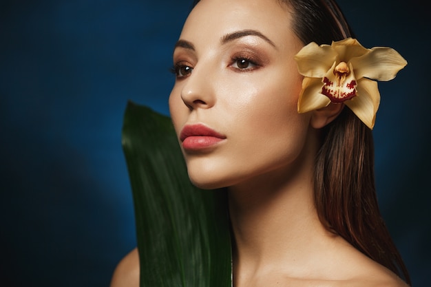 Foto gratuita closeup retrato de mujer con el pelo peinado hacia atrás, tierna flor de lirio detrás de la oreja. mirando a otro lado. concepto de belleza