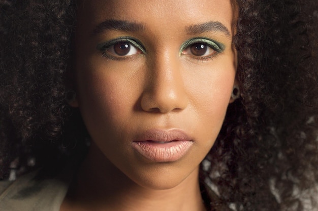 Closeup retrato s de joven modelo de raza mixta con pelo rizado en estudio con sombras de ojos metálicas verdes