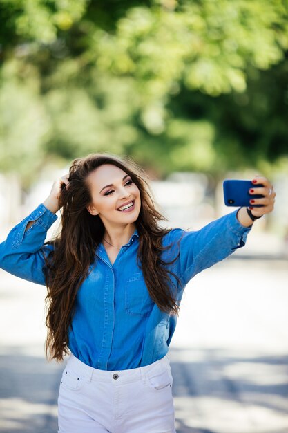 Closeup selfie-retrato estudiante de chica atractiva en gafas de sol con peinado largo y sonrisa blanca como la nieve en la ciudad.