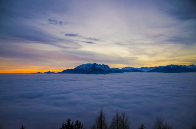Cloudscape rodeado de montañas rocosas cubiertas de nieve durante la puesta de sol en Suiza