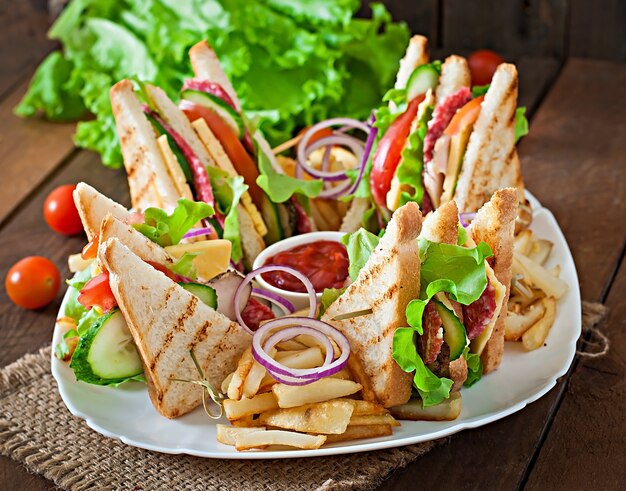 Club sandwich con queso, pepino, tomate, carne ahumada y salami. Servido con papas fritas.