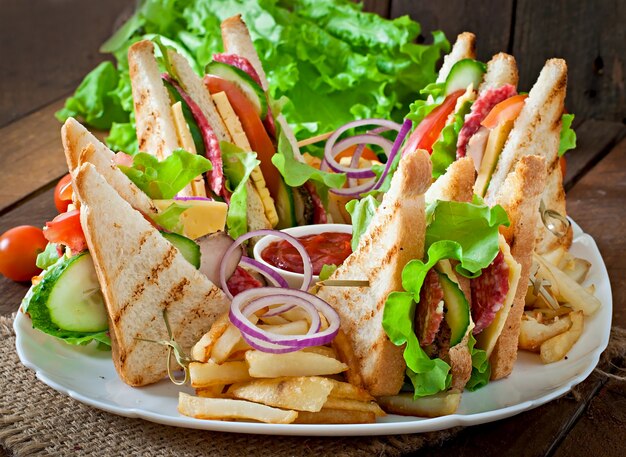 Club sandwich con queso, pepino, tomate, carne ahumada y salami. Servido con papas fritas.