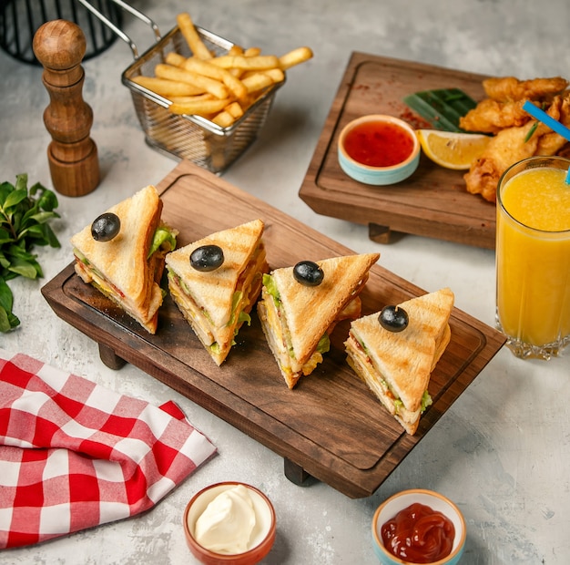 Club sándwiches en una tabla de madera con papas fritas y jugo de naranja.