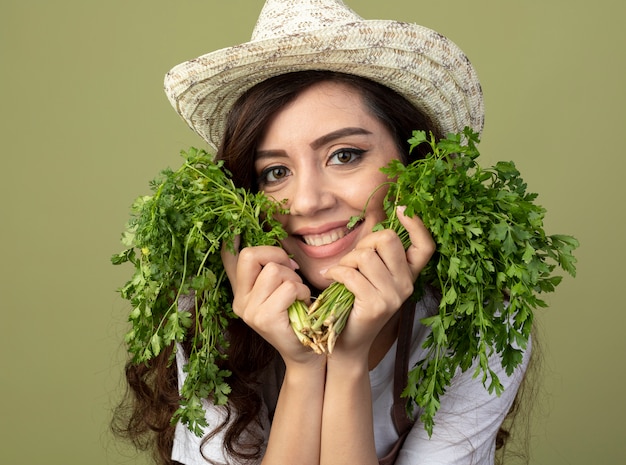 Cmiling joven jardinero en uniforme vistiendo sombrero de jardinería tiene cilantro en verde oliva