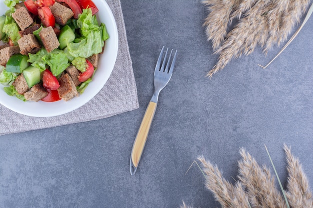 Cobertura de corteza seca en un plato de ensalada de pastor junto a un tenedor y tallos de pasto en la superficie de mármol