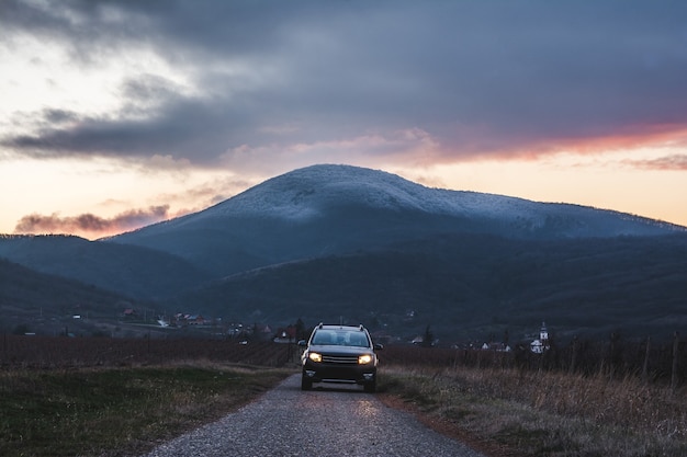 Coche en la carretera con una montaña durante la puesta de sol.