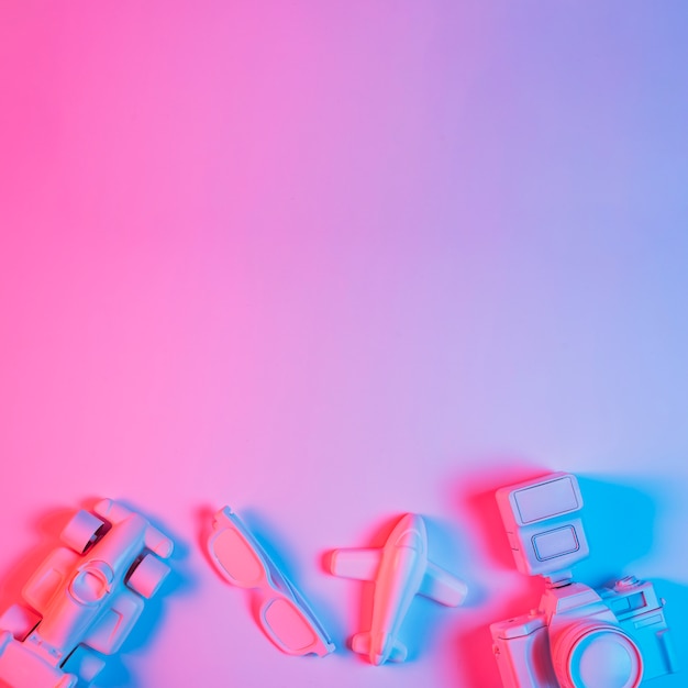 Coche de juguete; avión; Espectáculo y cámara dispuestos en el fondo de un fondo rosa con luz azul.