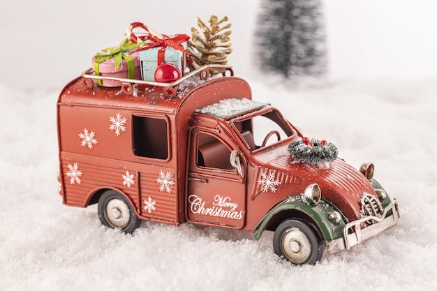 Coche de juguete pequeño decorado con adornos sobre nieve artificial con un árbol de Navidad en el fondo