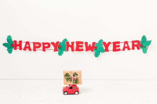 Coche de juguete con regalo cerca de feliz año nuevo inscripción