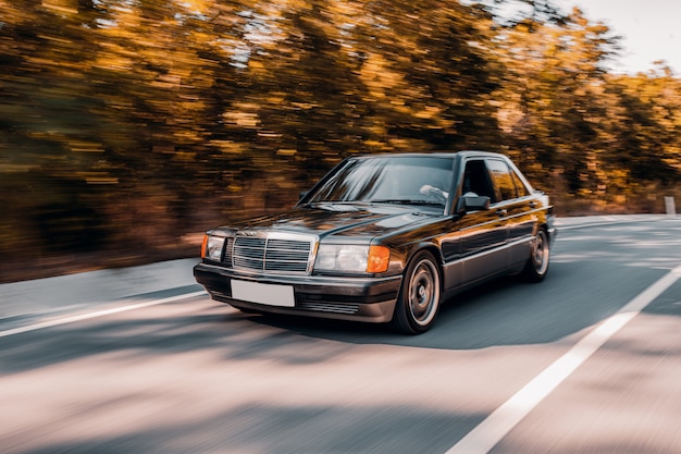 Foto gratuita un coche negro vintage conduciendo en la carretera anhelando a través del bosque.