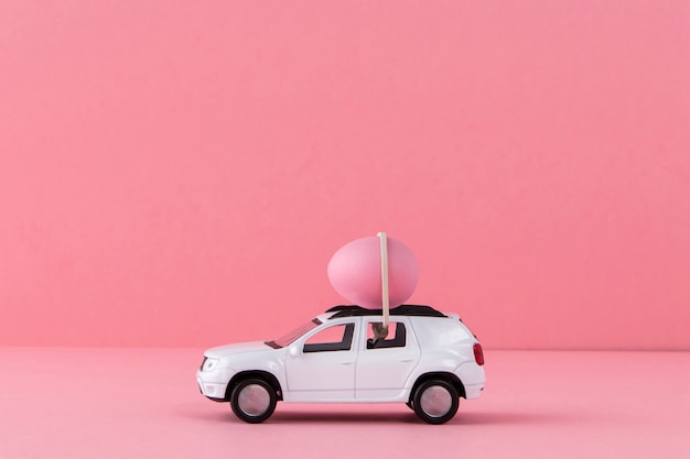 Coche de pascua blanco con huevo rosa y fondo.