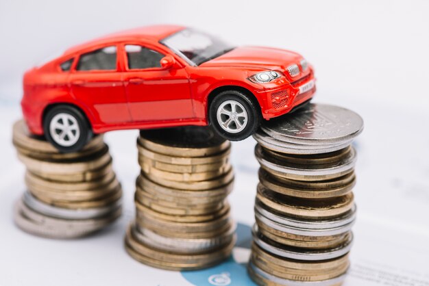 Coche rojo pequeño sobre la pila de monedas en aumento