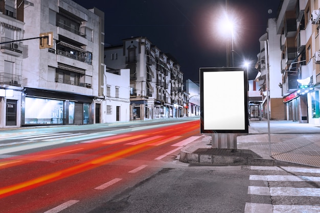 Coches senderos de luz que pasan cerca de la cartelera en blanco en la acera de la ciudad