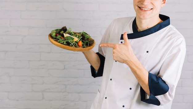 Cocinar el dedo acusador en ensalada fresca en plato de madera