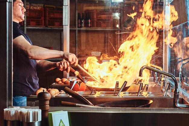 Cocinar es freír verduras con especias y salsa en un wok sobre una llama. Proceso de cocción en un restaurante asiático.