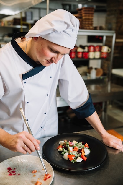 Cocinar poniendo tomate en un plato con ensalada.