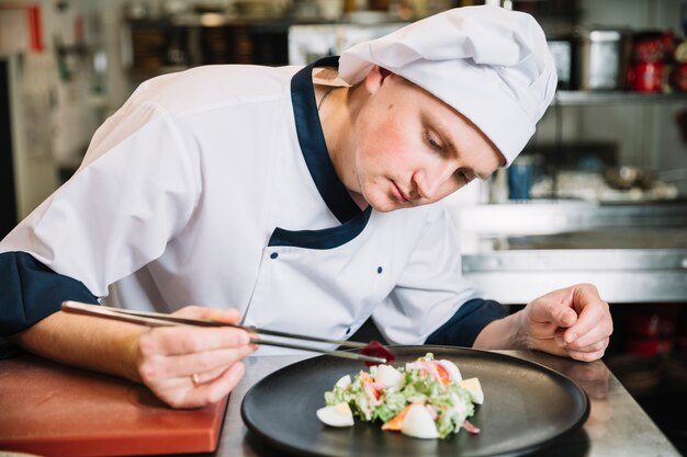 Cocinar poniendo verdura en plato con ensalada.