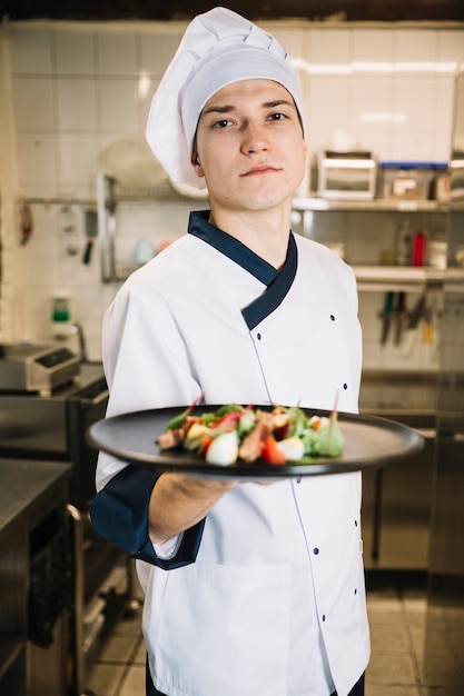 Foto gratuita cocinar sosteniendo ensalada con carne en un plato grande.