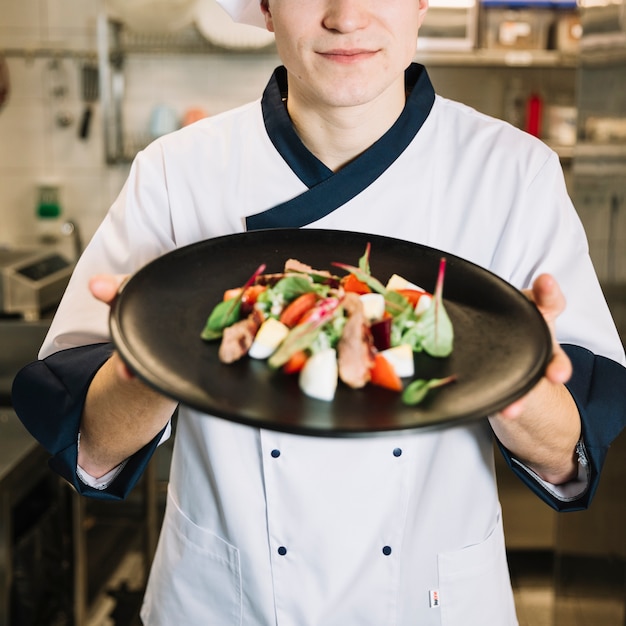 Cocinar sosteniendo ensalada con carne en plato negro