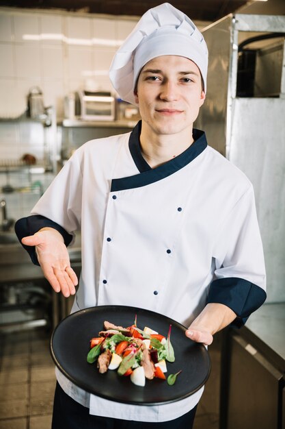 Cocinar sosteniendo ensalada con carne en plato