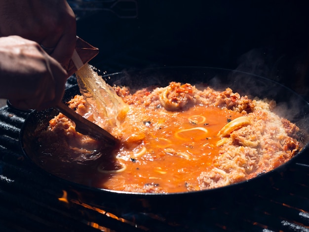 Cocine agregando salsa al arroz con aros de calamares y verduras en la sartén