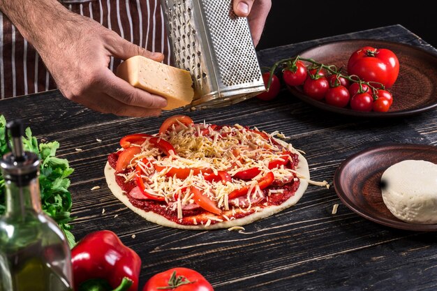 Cocine en la cocina poniendo los ingredientes en la pizza sobre un fondo de madera antiguo. concepto de pizza. Producción y entrega de alimentos. Concepto de cocina. De cerca