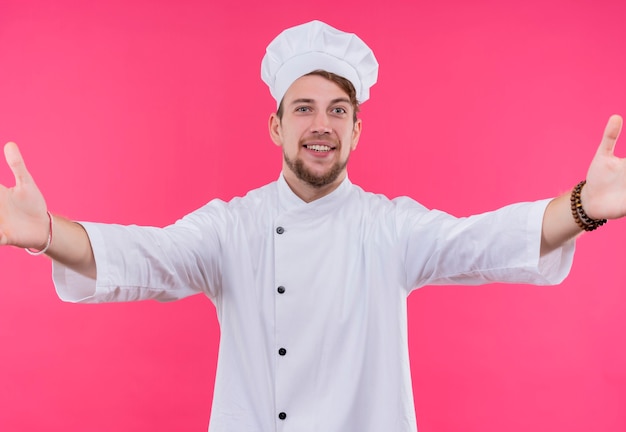 Cocine mirando a la cámara sonríe en la cara haciendo gesto de abrazo de pie sobre la pared rosa