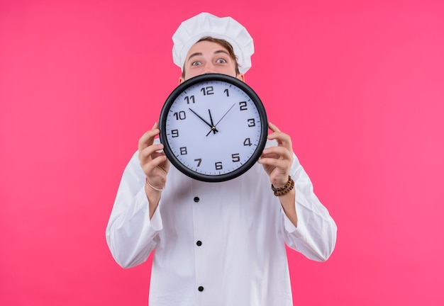 Cocine mirando a la cámara sorpresa en la cara que muestra el reloj parado sobre la pared rosa