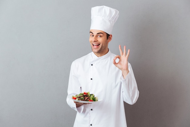 Cocine en uniforme con ensalada mostrando gesto bien.