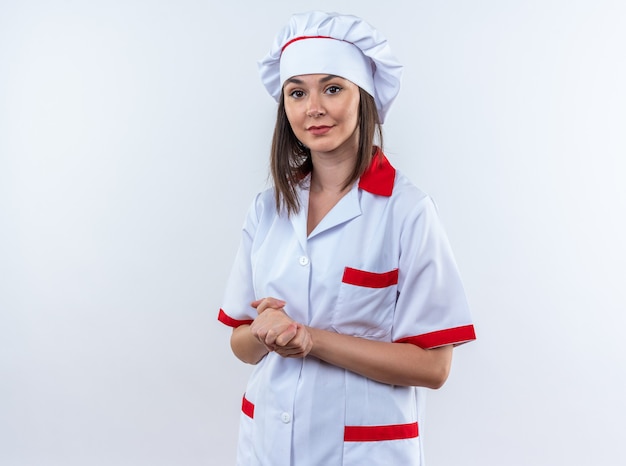 Cocinera joven complacida vistiendo uniforme de chef mostrando gesto de apretones de manos aislado sobre fondo blanco.