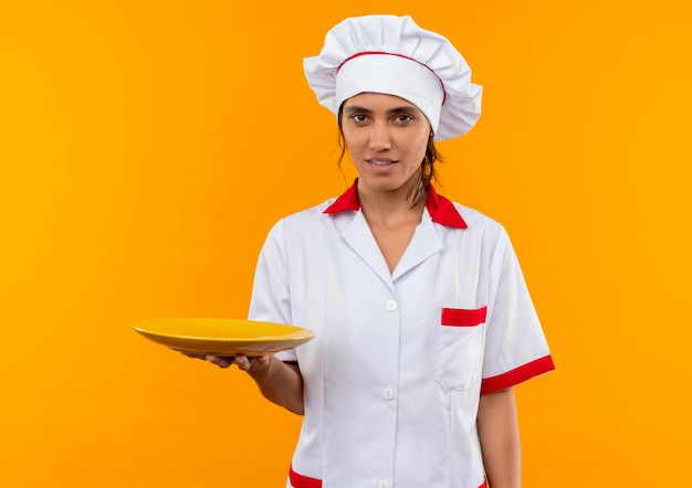 Cocinera joven complacida vistiendo uniforme de chef sosteniendo la placa con espacio de copia