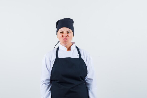 Cocinera en uniforme, delantal frunciendo el ceño mientras mira a la cámara, vista frontal.