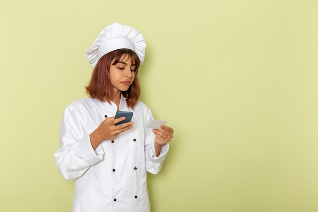 Cocinera de vista frontal en traje de cocinero blanco con su teléfono inteligente en la superficie verde