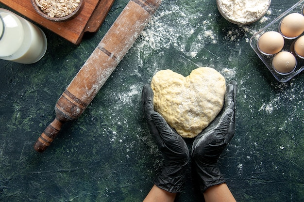 Foto gratuita cocinera de vista superior trabajando con masa en forma de corazón sobre superficie gris oscuro