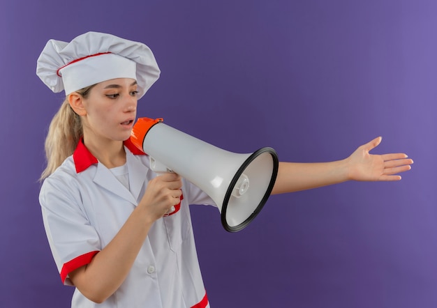 Cocinero bastante joven en uniforme de chef estirando la mano al lado y hablando por altavoz