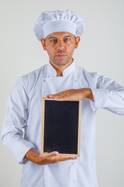 Cocinero chef hombre sosteniendo la pizarra y mirando a la cámara con sombrero y uniforme