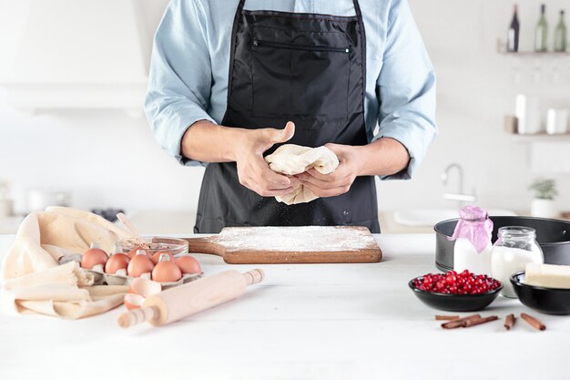Un cocinero en una cocina rústica. Las manos masculinas con ingredientes para cocinar productos de harina o masa, pan, magdalenas, pastel, pastel, pizza