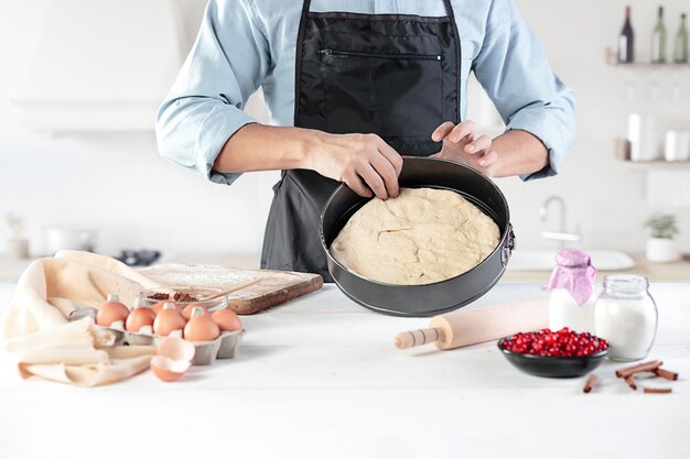 Un cocinero en una cocina rústica. Las manos masculinas con ingredientes para cocinar productos de harina o masa, pan, magdalenas, pastel, pastel, pizza