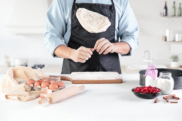 Un cocinero en una cocina rústica. las manos masculinas con ingredientes para cocinar productos de harina o masa, pan, magdalenas, pastel, pastel, pizza