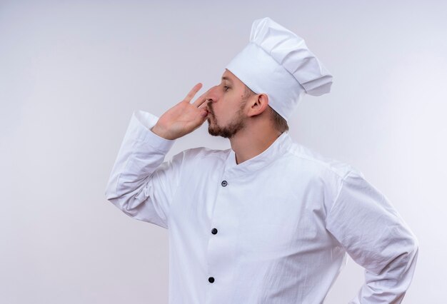 Cocinero cocinero masculino profesional satisfecho en uniforme blanco y sombrero de cocinero mostrando signo de pie delicioso sobre fondo blanco.