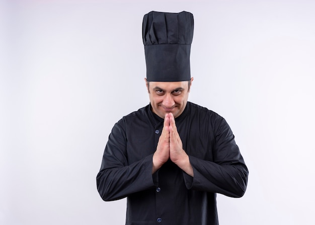 Cocinero cocinero masculino vistiendo uniforme negro y sombrero de cocinero tomados de la mano juntos sintiéndose agradecido de pie sobre fondo blanco.