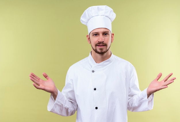 Cocinero cocinero profesional masculino en uniforme blanco y sombrero de cocinero extendiendo las manos sonriendo amable de pie sobre fondo verde