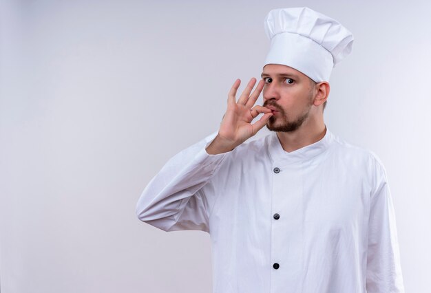 Cocinero cocinero profesional masculino en uniforme blanco y sombrero de cocinero que muestra el signo de pie delicioso sobre fondo blanco