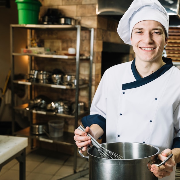 Cocinero feliz azotando algo en una olla con batidor