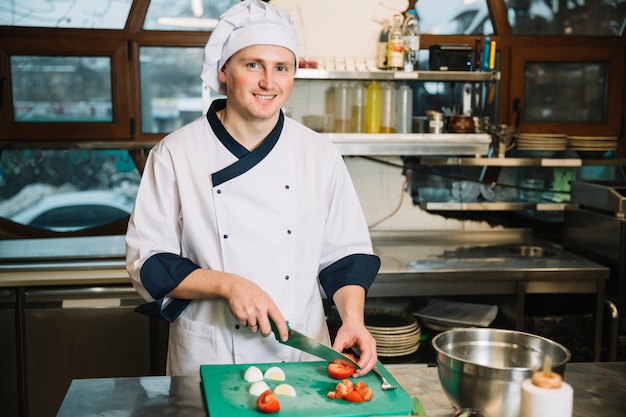 Cocinero feliz cortando tomate a bordo