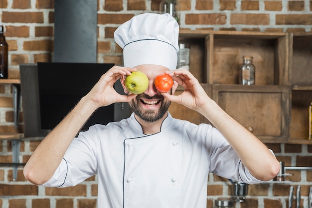 Cocinero feliz con manzana y tomate rojo frente a sus ojos