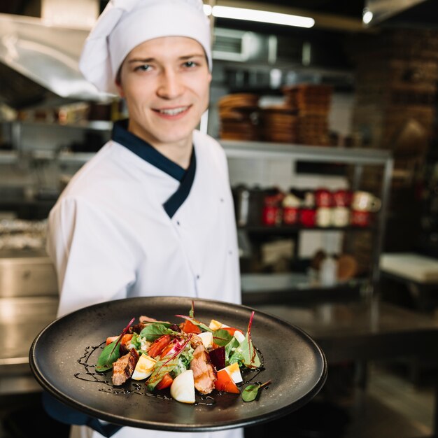 Cocinero feliz mostrando ensalada con carne en plato